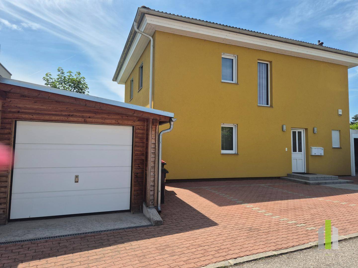 Vorderansicht des gelben Hauses mit separater Garage und gepflasterter Einfahrt.