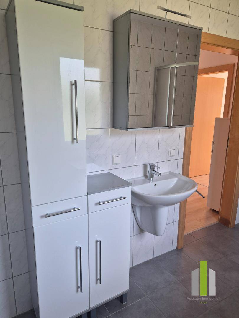 Modernes Badezimmer mit Waschbecken, Hochschrank und Spiegelschrank, hell gefliest und funktional.