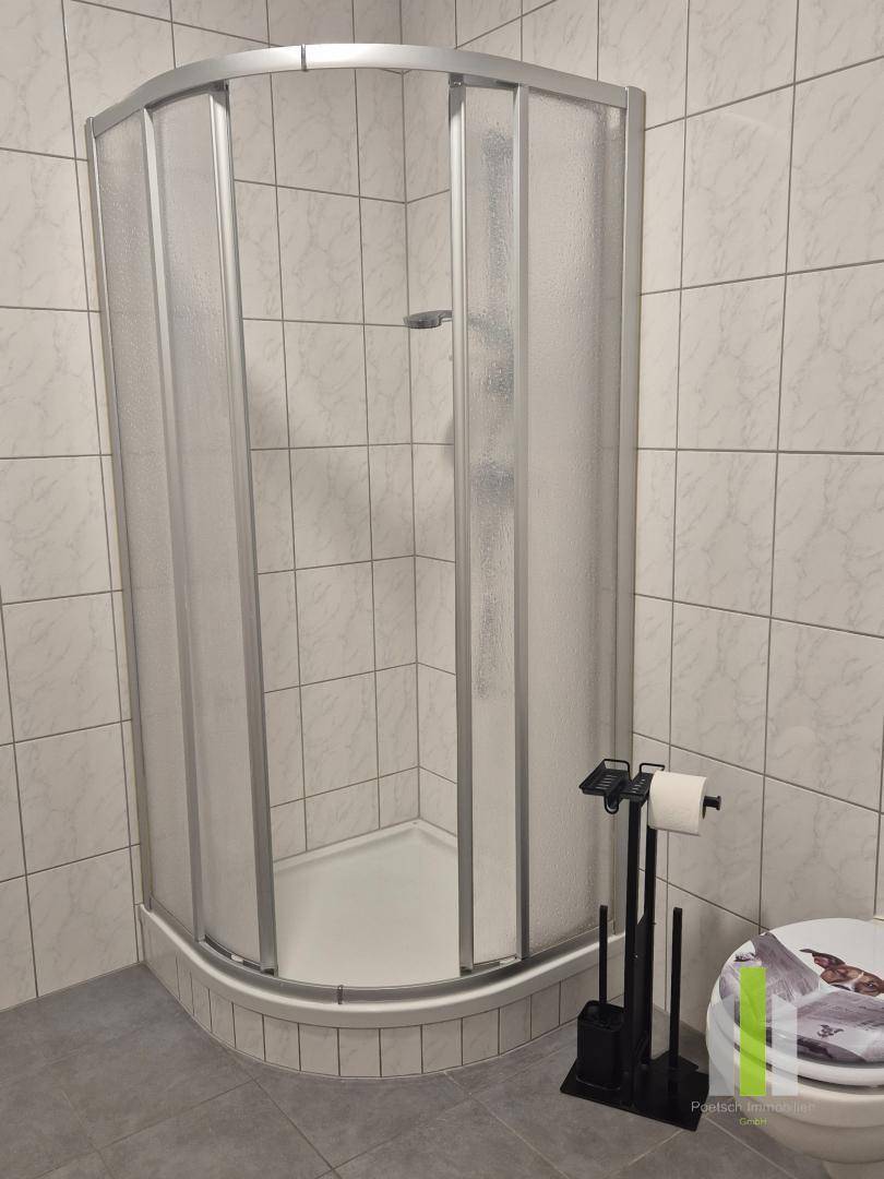Badezimmer mit Eckduschkabine, hellen Fliesen an Wänden und dunklem Boden, funktional und sauber.
