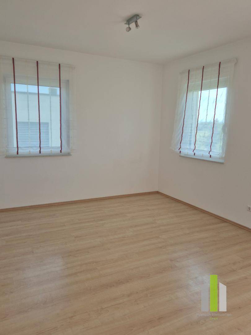 Leerer Raum mit Laminatboden und zwei Fenstern, sorgt für eine helle und freundliche Atmosphäre.