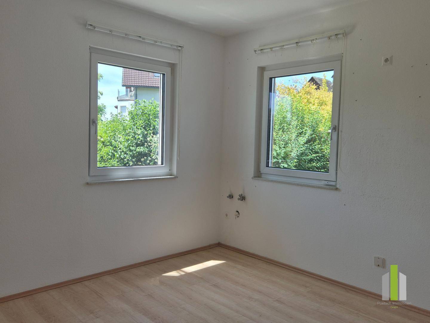 Heller Raum mit Laminatboden und zwei Fenstern, möglicherweise für eine Küche oder einen Hauswirtschaftsraum vorgesehen.