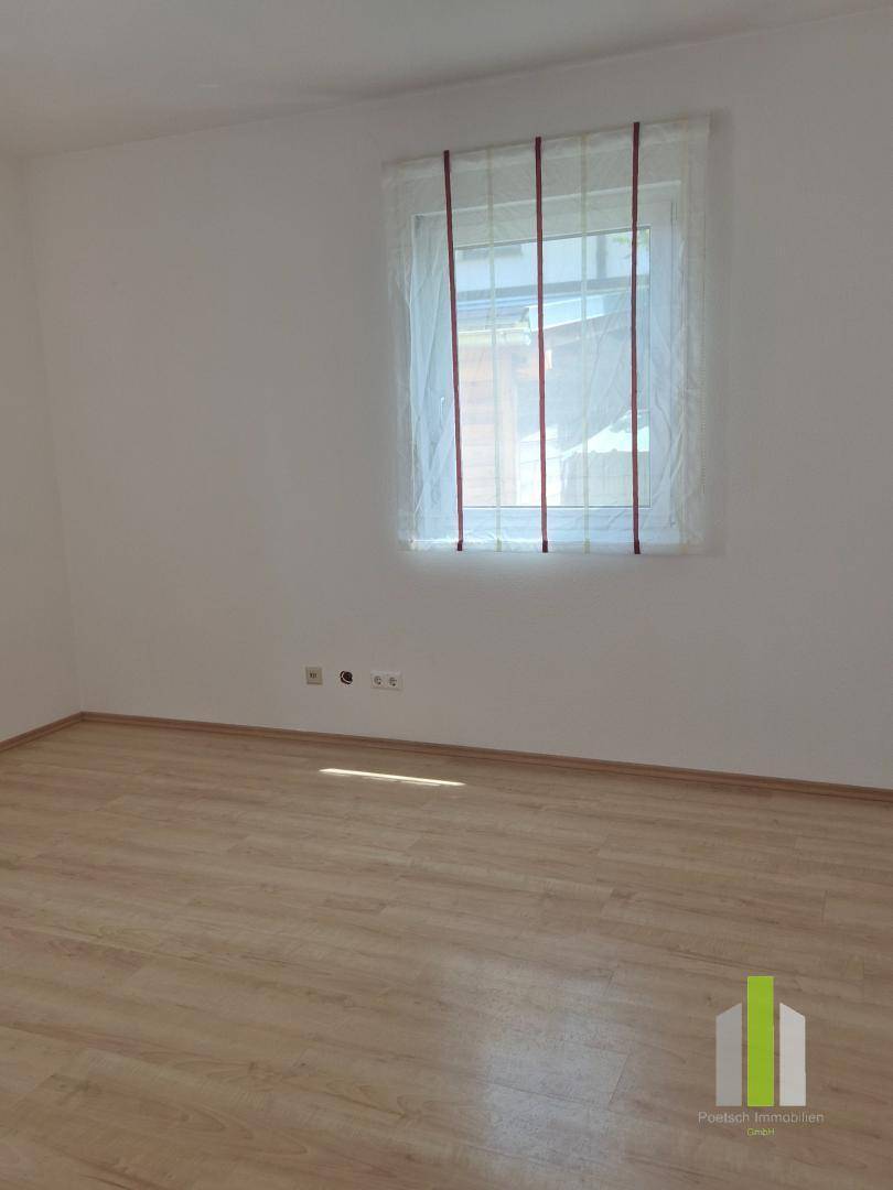 Leerer Raum mit Laminatboden und einem Fenster, bietet ausreichend Tageslicht für verschiedene Wohnzwecke.