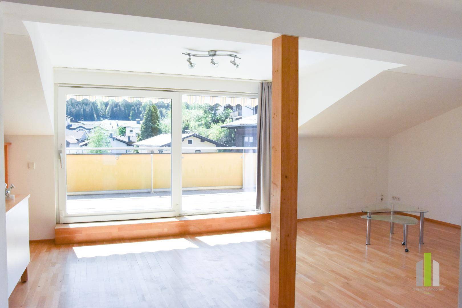 Lichtdurchfluteter Wohnbereich mit Holzboden, Dachschrägen und großem Fenster zum Balkon.