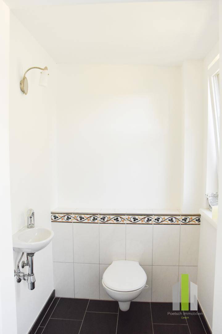 Kleines Gäste-WC mit WC, Waschbecken und dekorativen Fliesenbordüren.