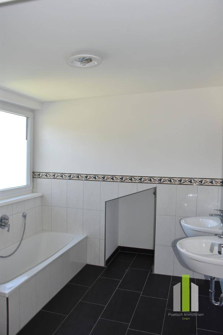 Helles Badezimmer mit Badewanne, Doppelwaschbecken und dekorativen Fliesen.