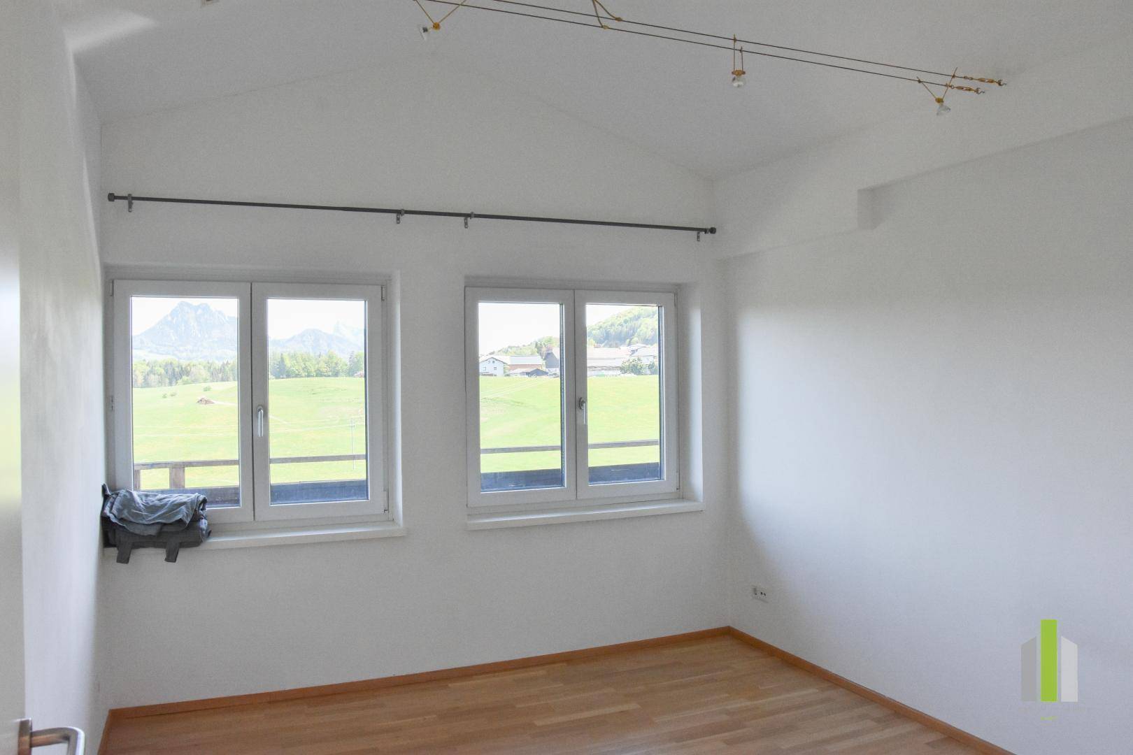 Helles Schlafzimmer mit Holzboden, Dachschrägen und Panoramablick auf die Landschaft.