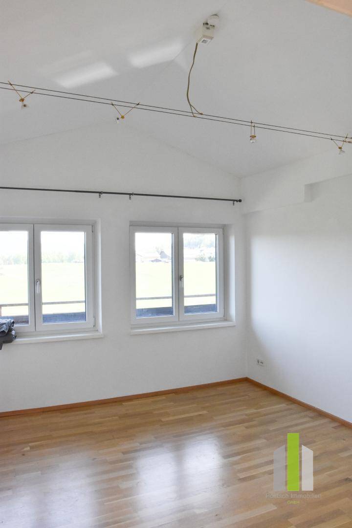 Geräumiges Zimmer mit Holzboden, Dachschrägen und zwei Fenstern mit weitem Ausblick.