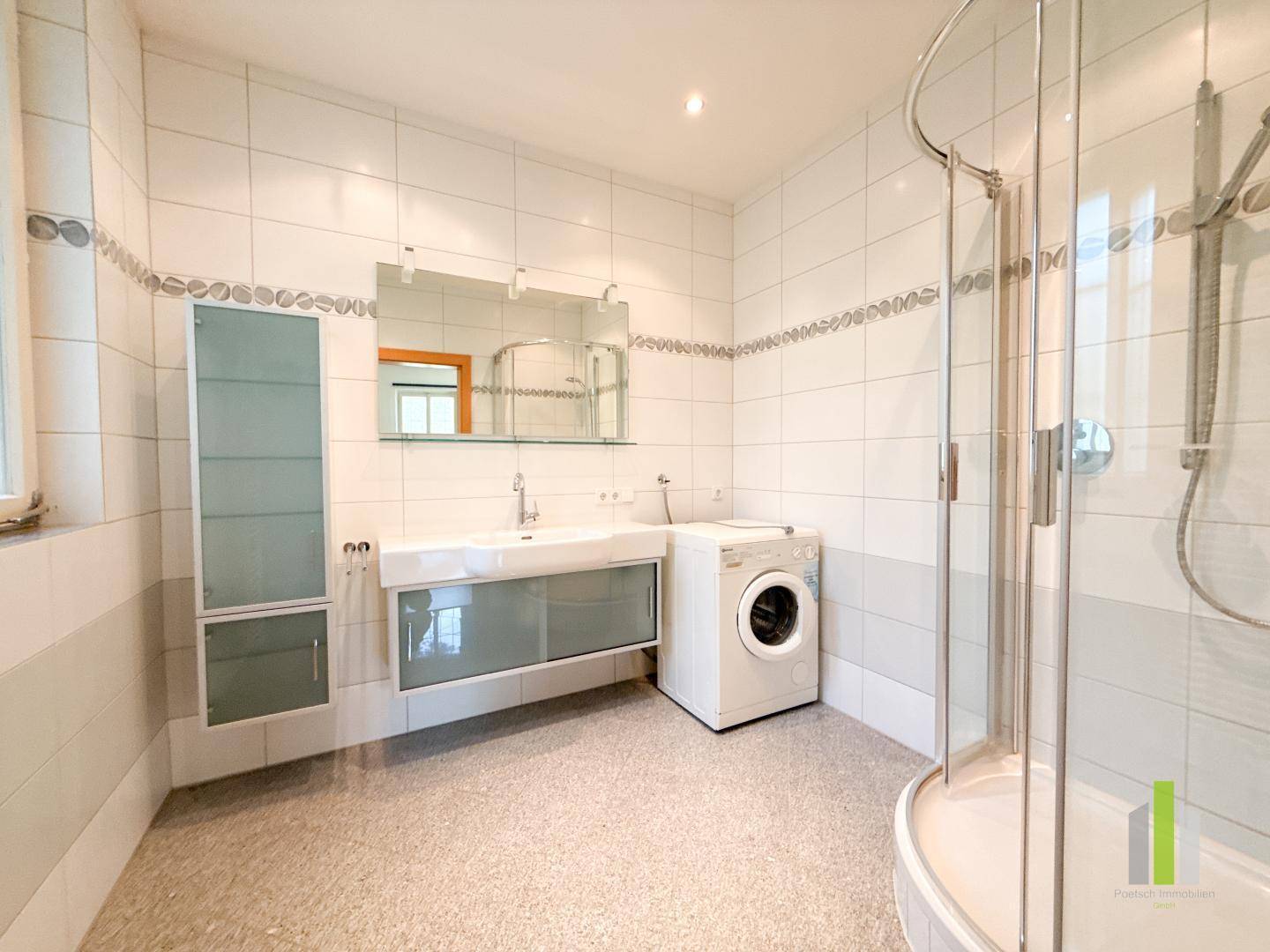 Helles Badezimmer mit Dusche, Waschmaschine und großem Waschtisch.