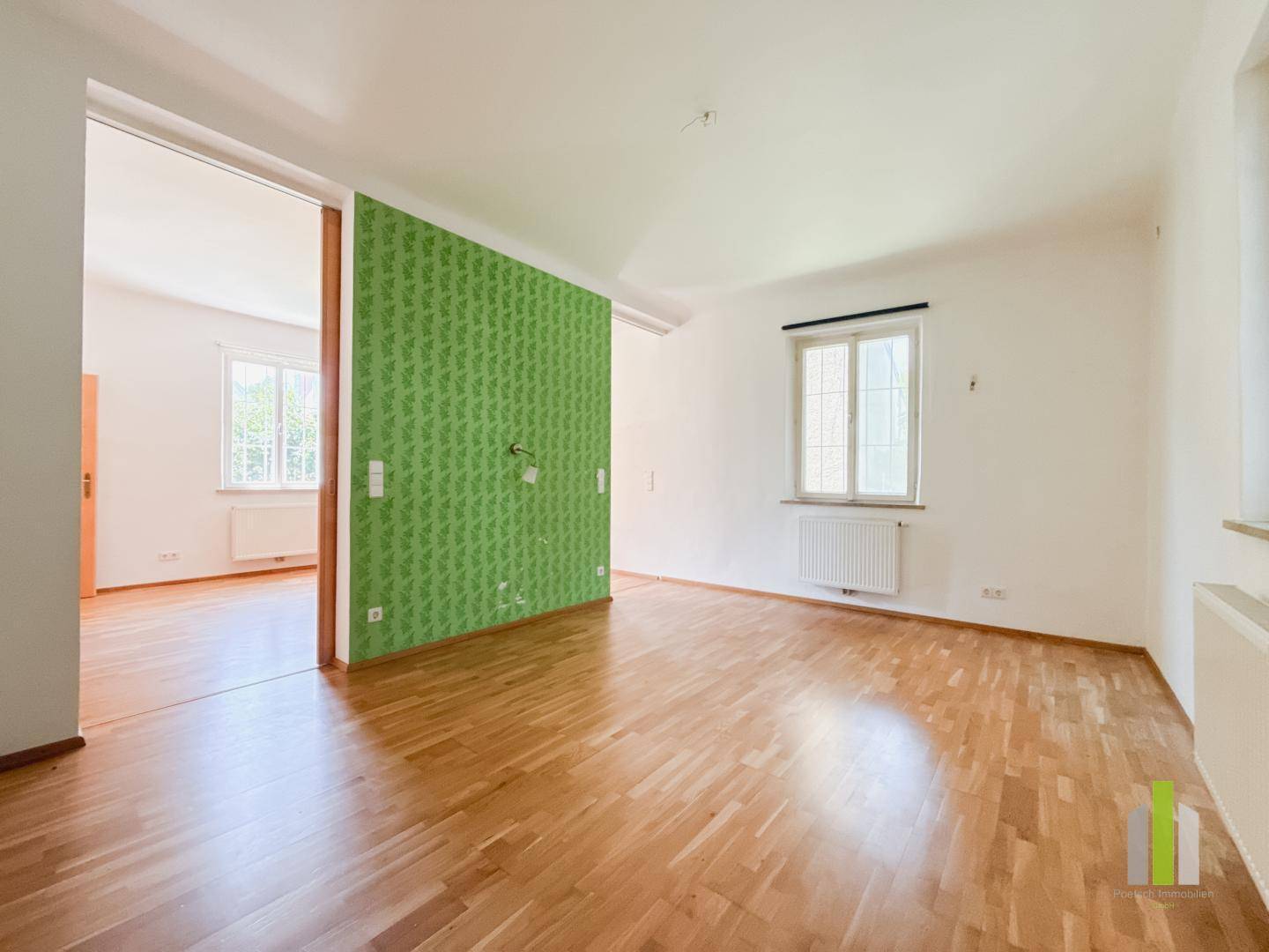Geräumiges Wohnzimmer mit Holzboden und einer grünen Akzentwand.