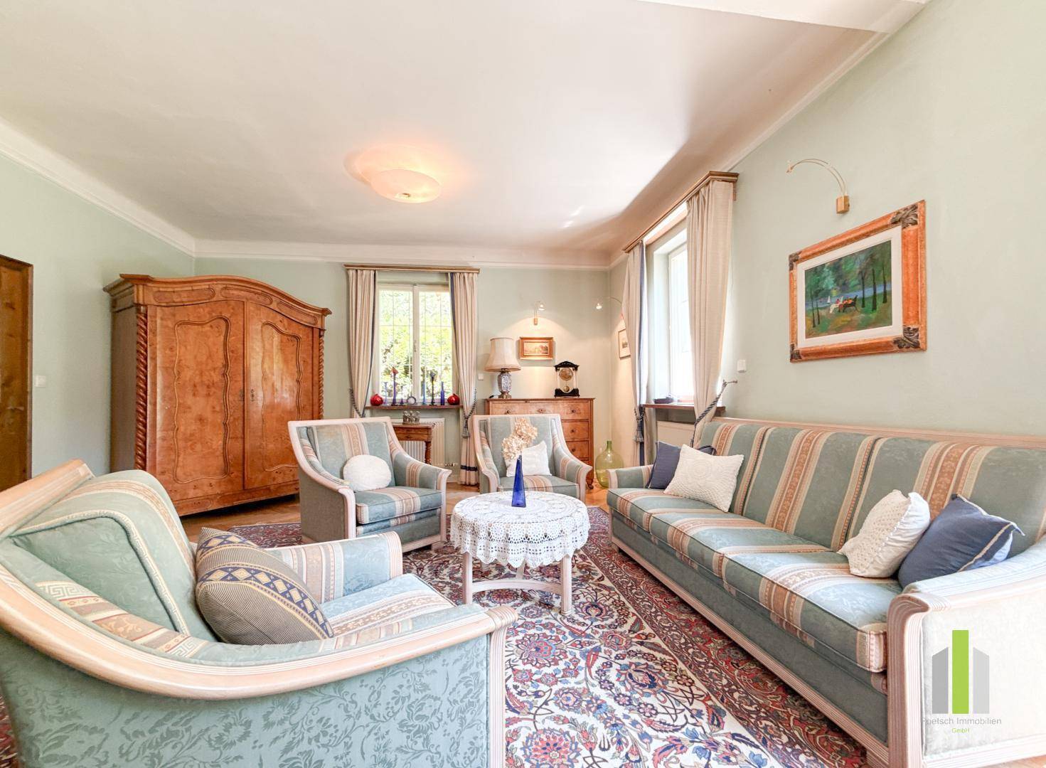 Elegantes Wohnzimmer mit hellgrünen Wänden, klassischen Sofas und einem großen Holzschrank.