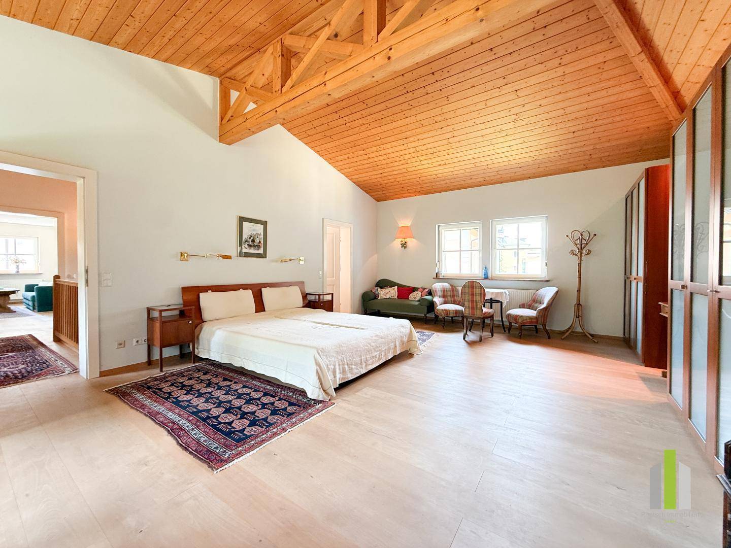 Großes Schlafzimmer im Dachgeschoss mit Holzbalkendecke, Holzboden und Doppelbett.