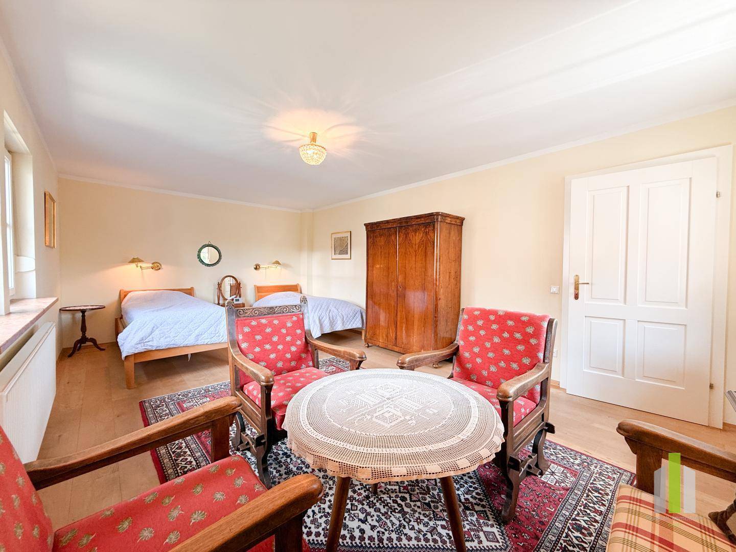 Helles Schlafzimmer mit zwei Einzelbetten, traditionellen Holzmöbeln und einem gemütlichen Sitzbereich am Fenster.