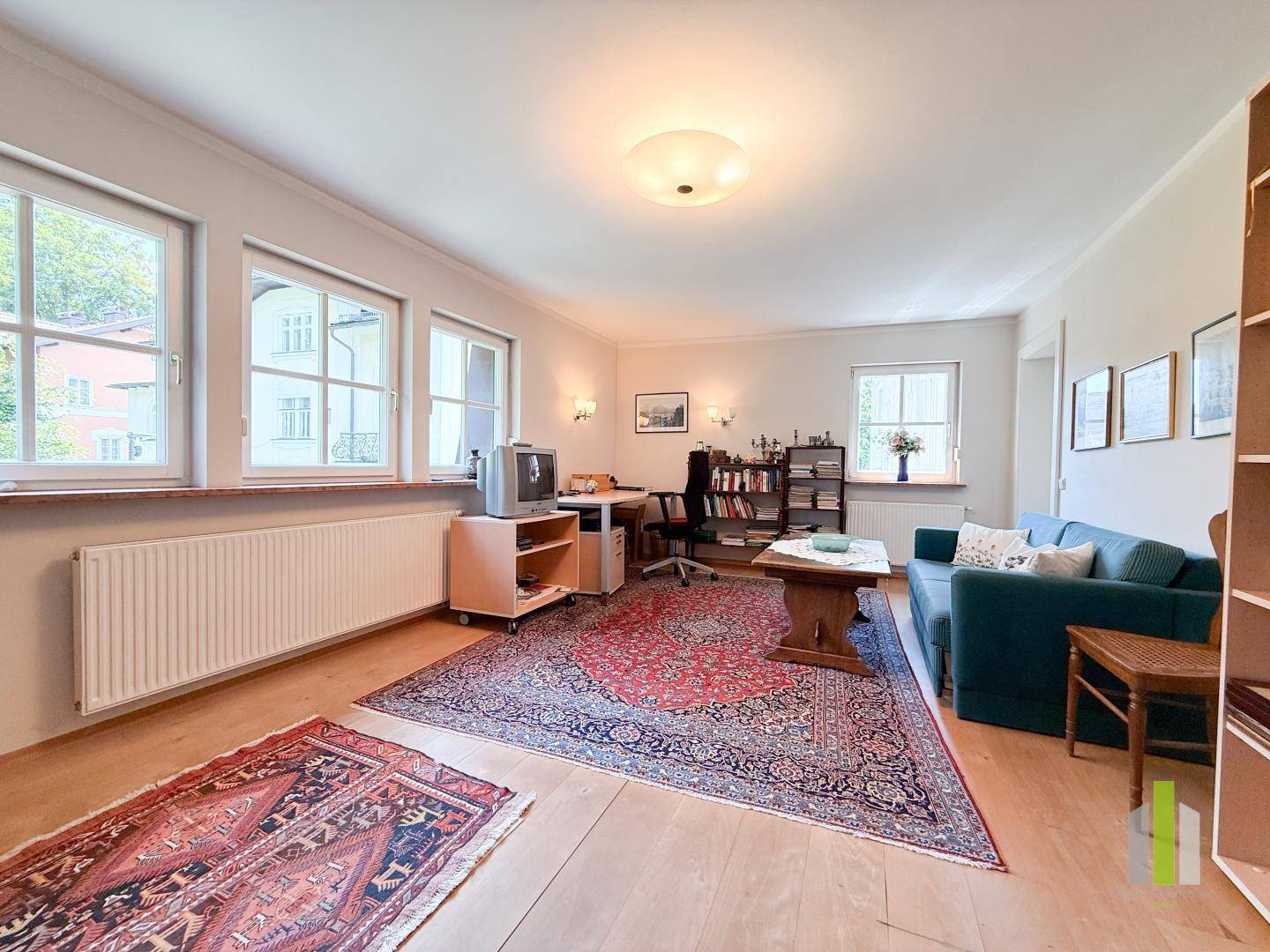 Helles Wohnzimmer mit Holzboden, Teppichen und mehreren Fenstern.