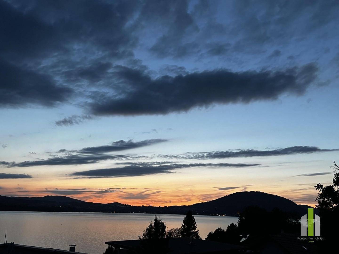 Sonnenuntergang über einem See mit Bergen im Hintergrund und dunklen Wolken am Himmel.