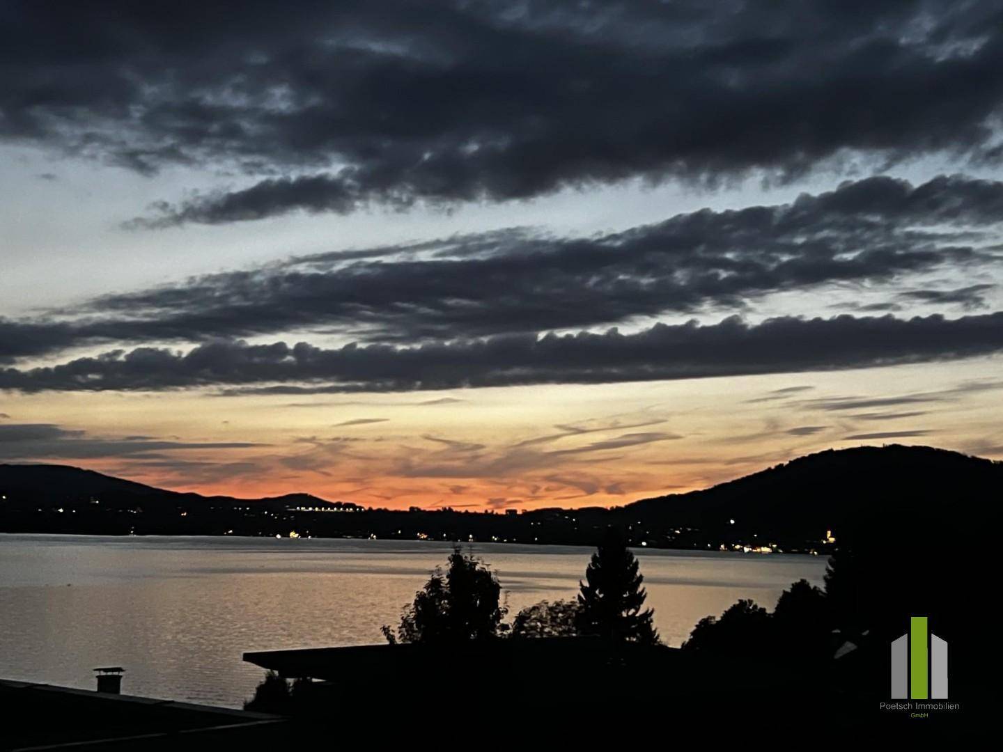 Atemberaubender Sonnenuntergang über dem See mit leuchtend orangefarbenem Himmel und dunklen Bergsilhouetten.