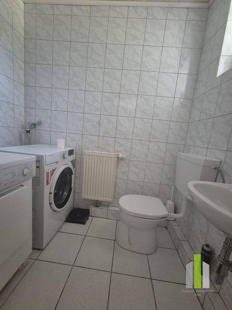 Praktischer Hauswirtschaftsraum mit Waschmaschine, Toilette und kleinem Waschbecken.