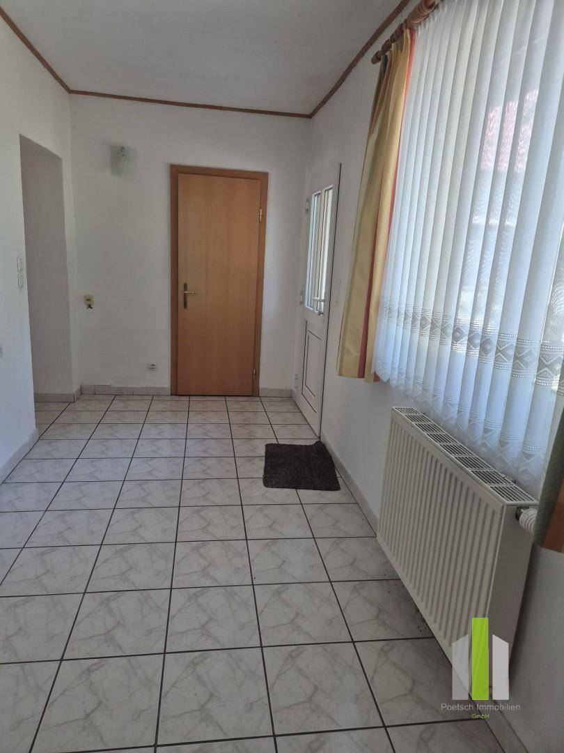 Heller Flur mit Fliesenboden, Heizkörper und Fenster mit Vorhängen.