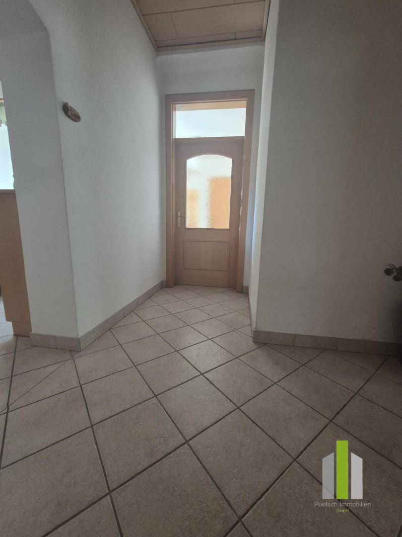 Heller Eingangsbereich mit Fliesenboden und Holztür mit Glaseinsatz.
