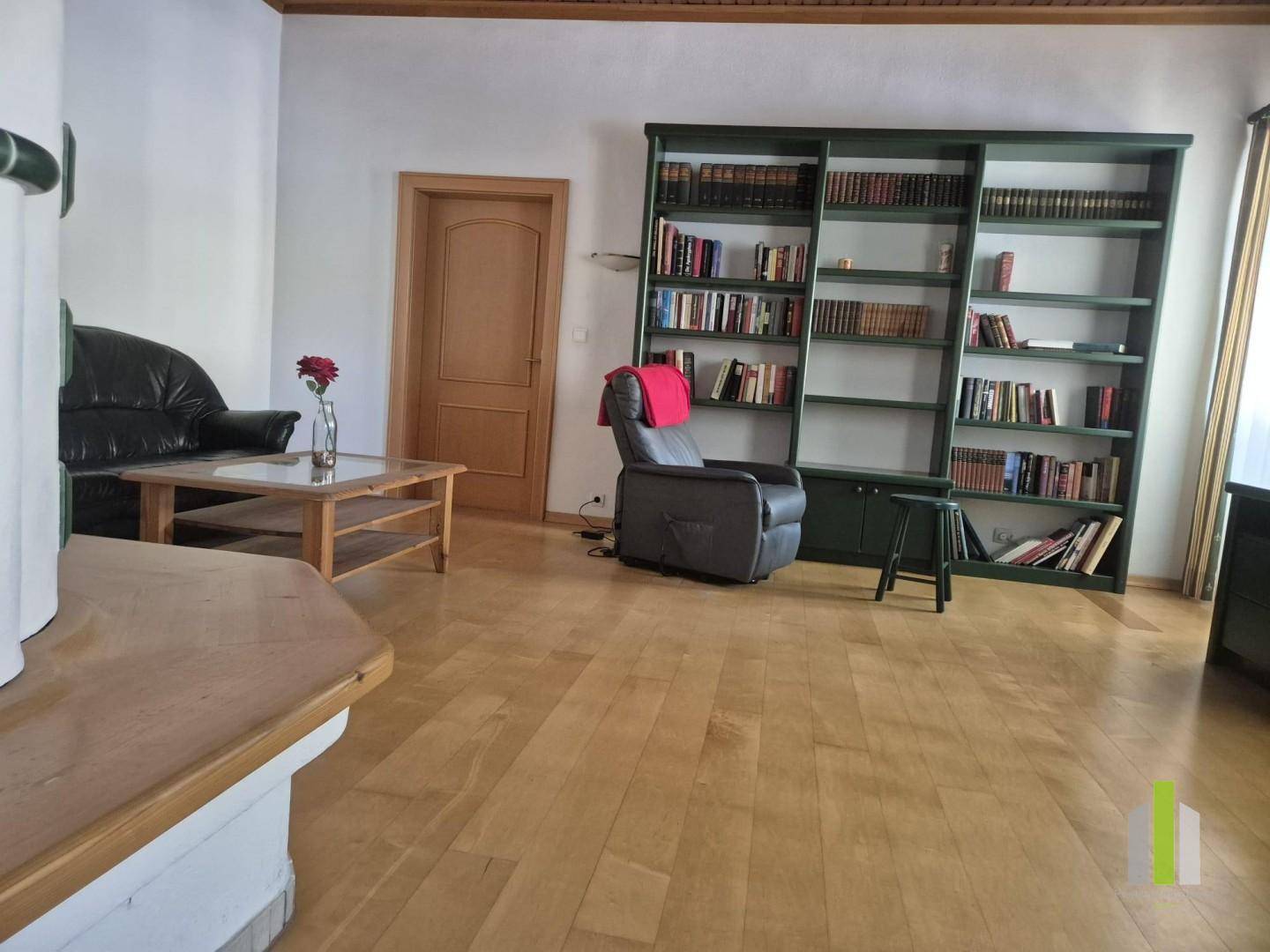 Geräumiges Wohnzimmer mit Holzboden, großem Bücherregal und bequemen Sesseln.