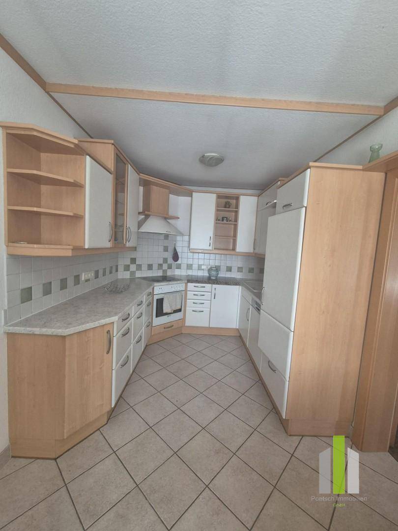 Funktionale Küche mit hellen Holzschränken, weißen Fronten und Fliesenboden.