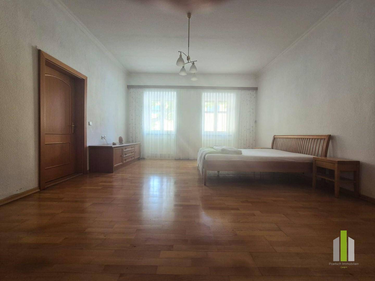 Helles Schlafzimmer mit Holzboden, Doppelbett und zwei Fenstern.