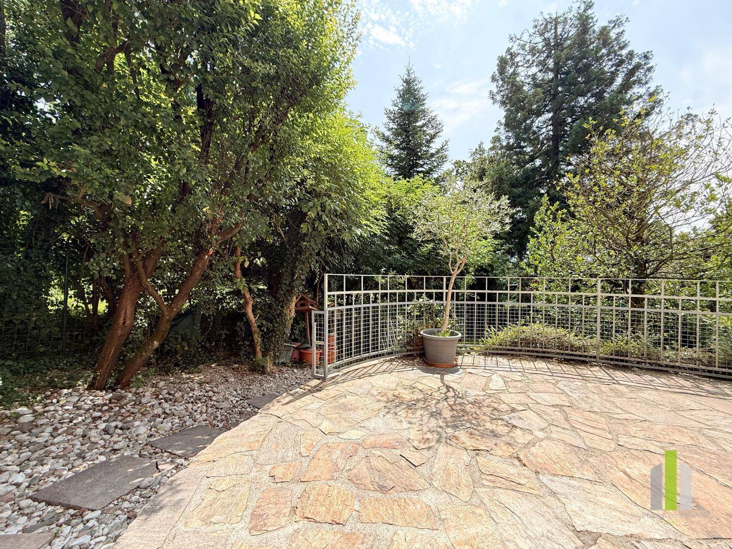 Große gepflasterte Terrasse mit Blick auf den Garten und alte Bäume im Hintergrund.