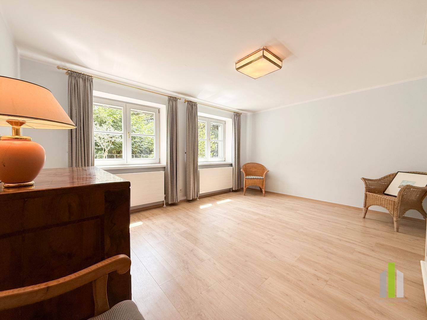Helles Zimmer mit Holzboden, Vorhängen und Blick in den grünen Garten, bereit zur Einrichtung.