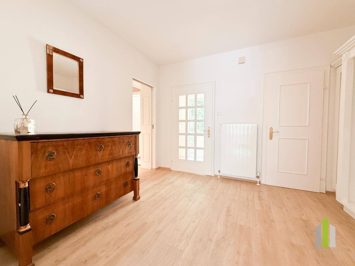 Heller Flur mit Holzboden, antiker Kommode und weißen Türen, die zu weiteren Räumen führen.