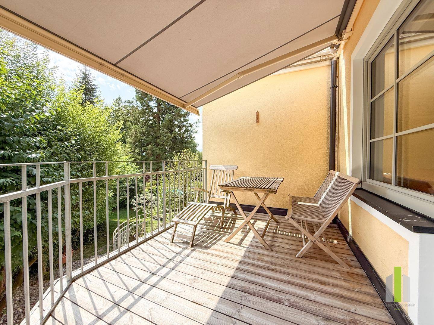 Überdachter Balkon mit Holzboden, Sitzgelegenheiten und Blick ins Grüne.