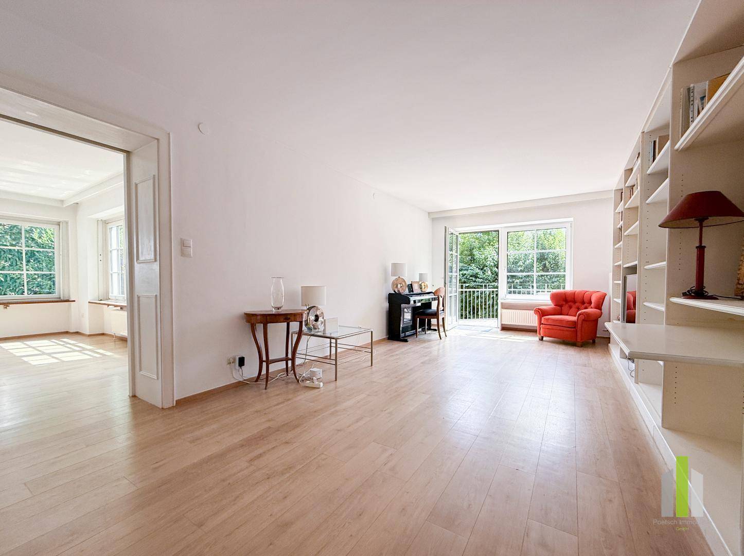 Helles Wohnzimmer mit Holzboden, Bücherregal und Zugang zu einem kleinen Balkon.