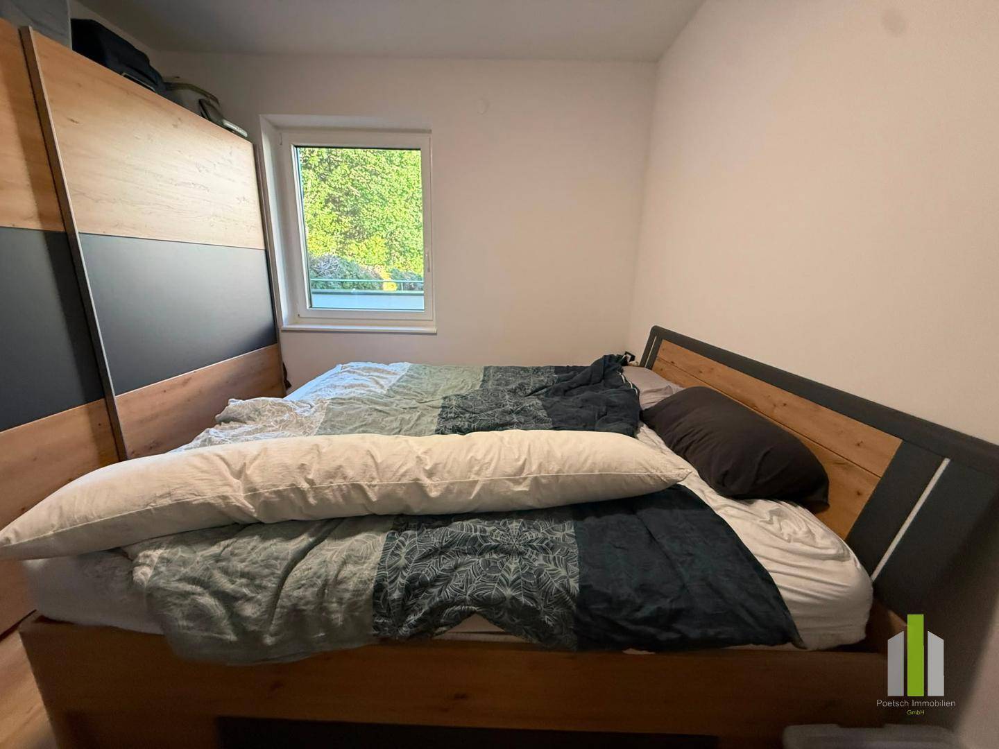 Gemütliches Schlafzimmer mit Holzbett, großem Kleiderschrank und Blick ins Grüne.