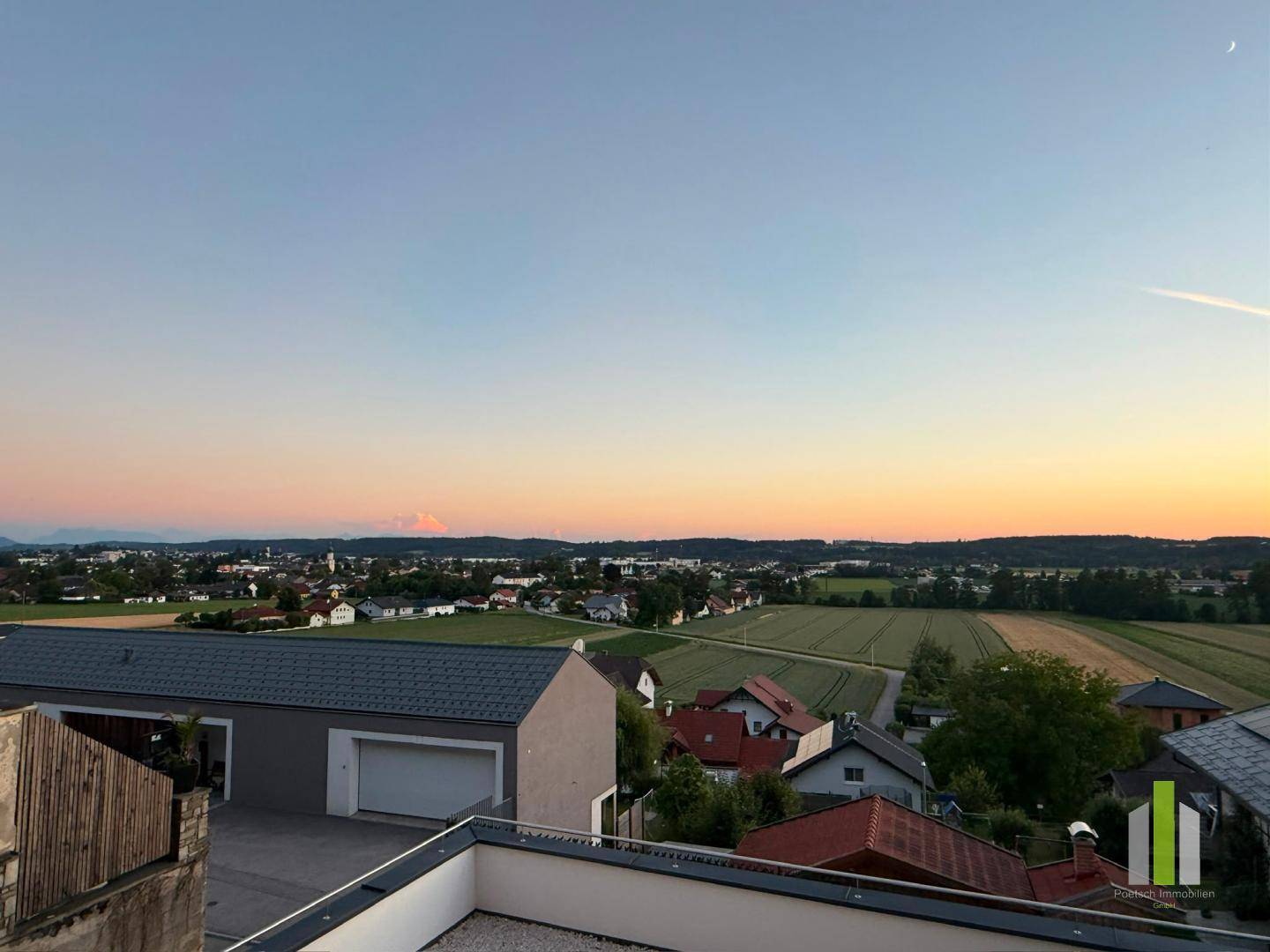 Weitläufiger Blick über die Landschaft und eine Stadt bei Sonnenuntergang mit Bergen am Horizont.