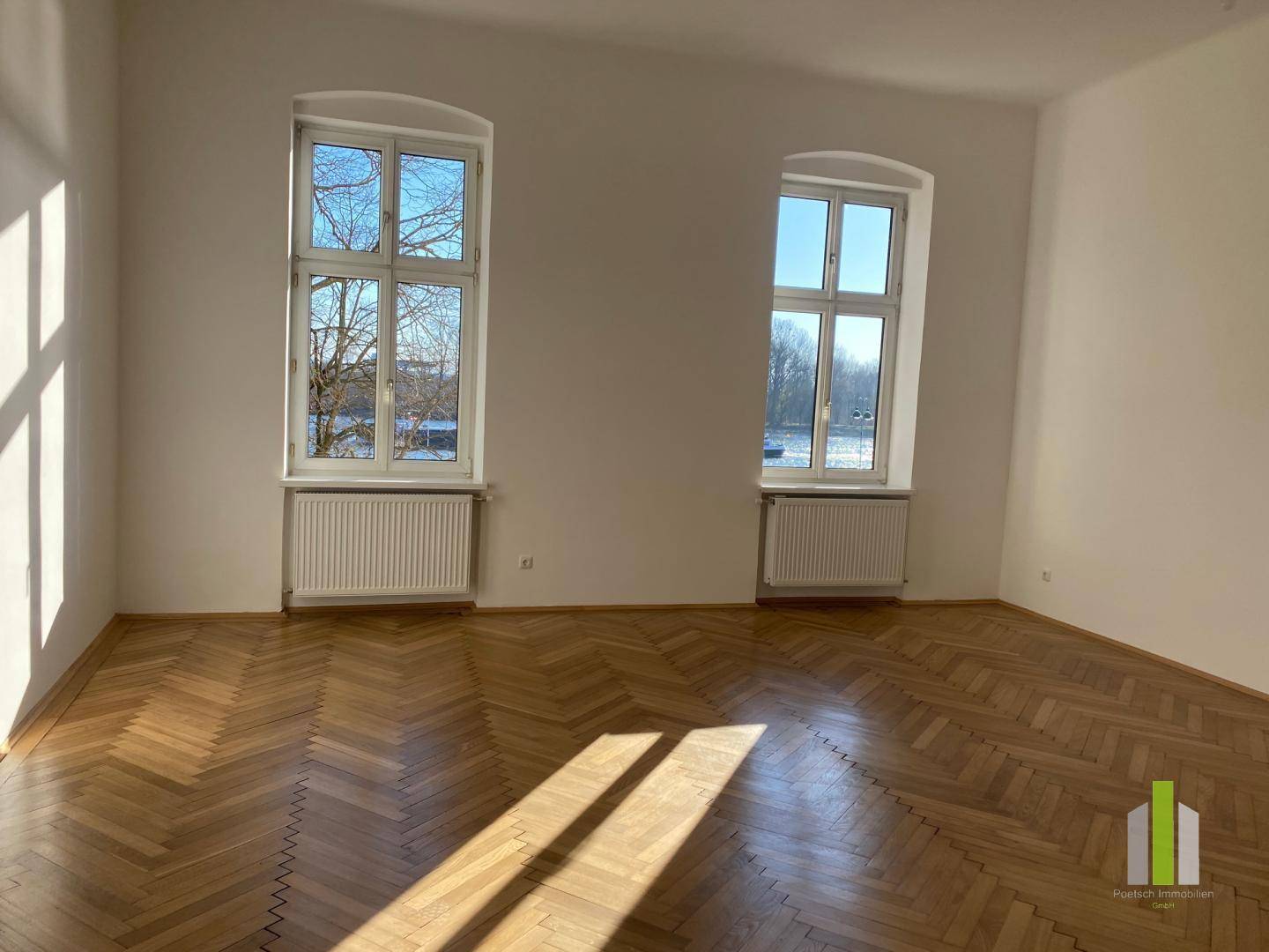 Helles Zimmer mit Fischgrätparkettboden, hohen Fenstern und viel natürlichem Licht.