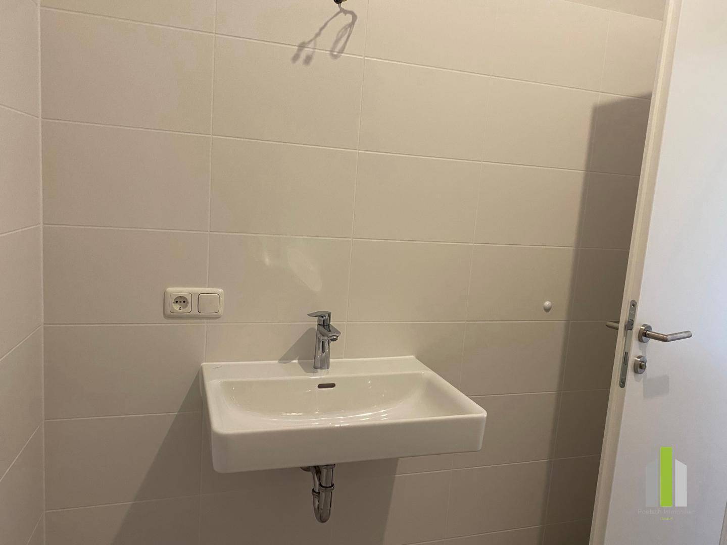 Modernes Badezimmer mit weißem Waschbecken und hellen Fliesen an den Wänden.