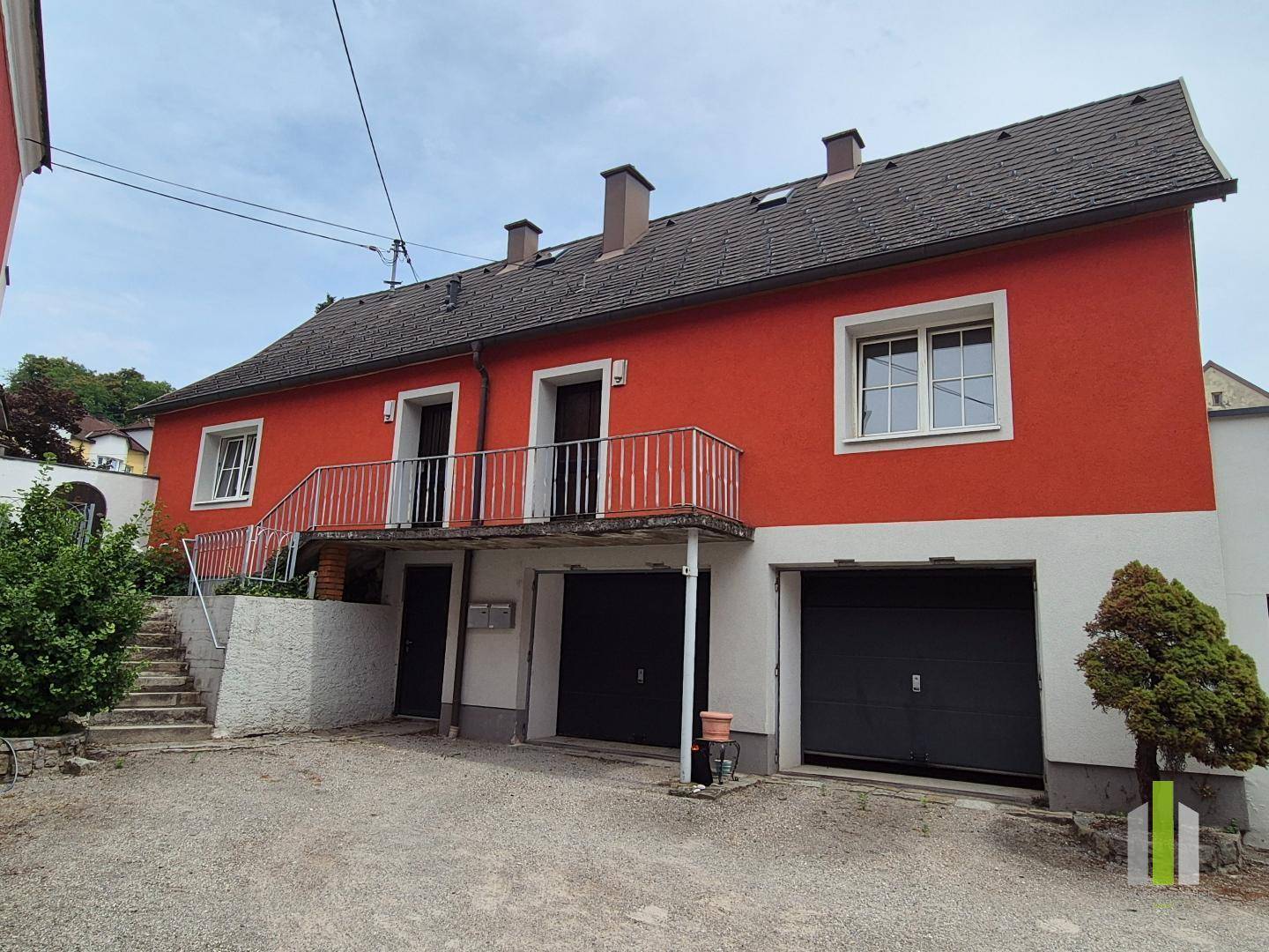 Rotes Gebäude mit Garagen, Außentreppe und einem Balkon mit Metallgeländer.
