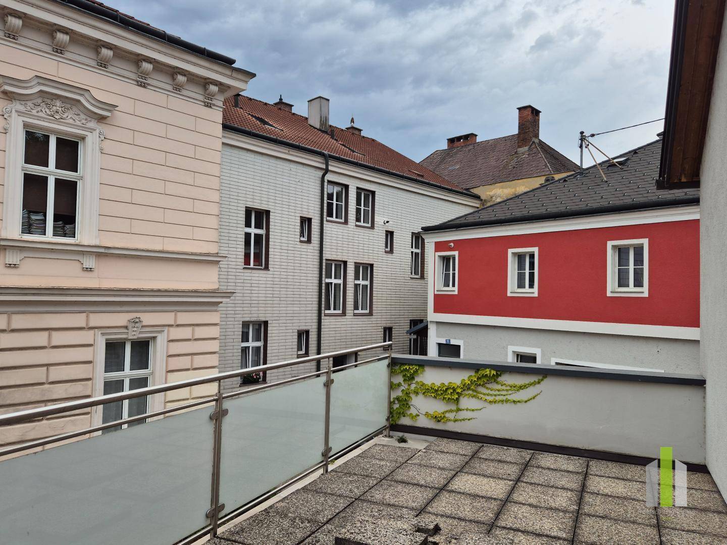 Geräumige Terrasse mit Glasgeländer und Blick auf umliegende historische Gebäude.