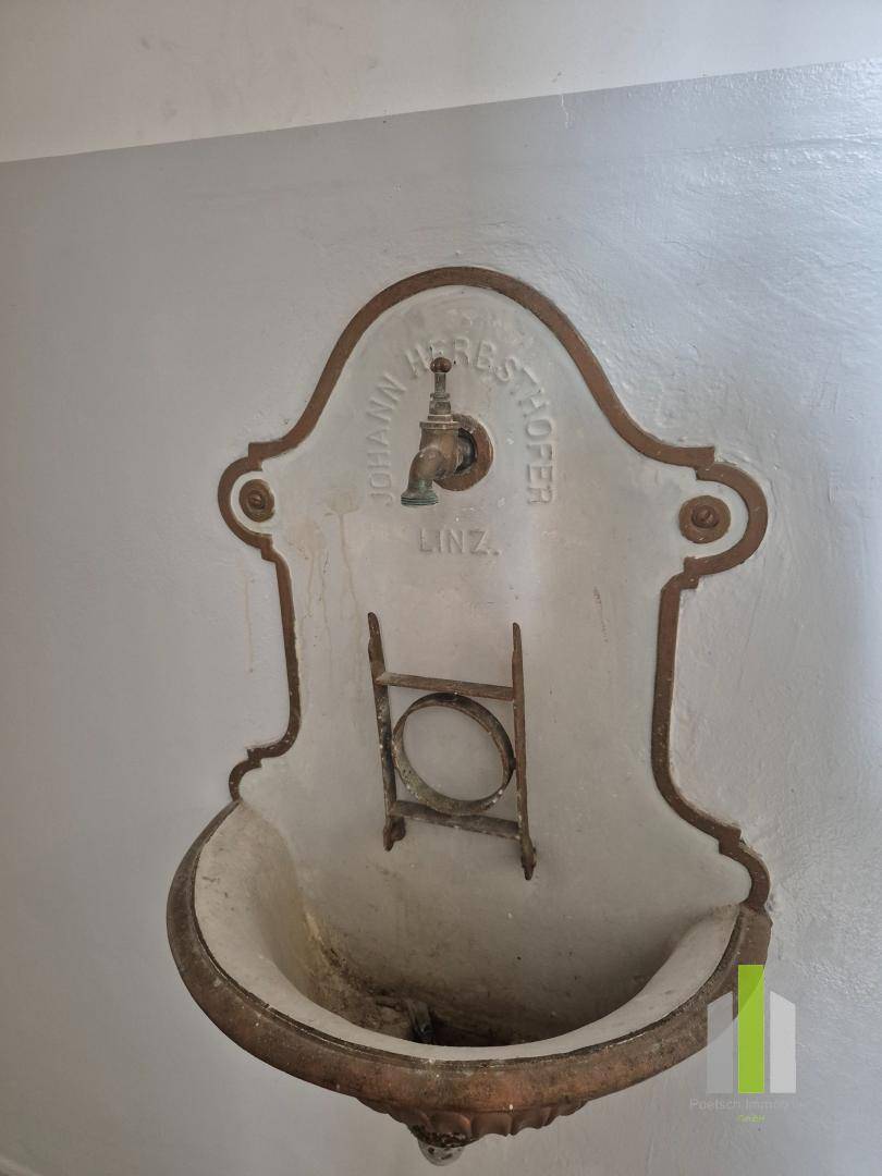 Historisches Wandwaschbecken mit Wasserhahn und dekorativer Einfassung.