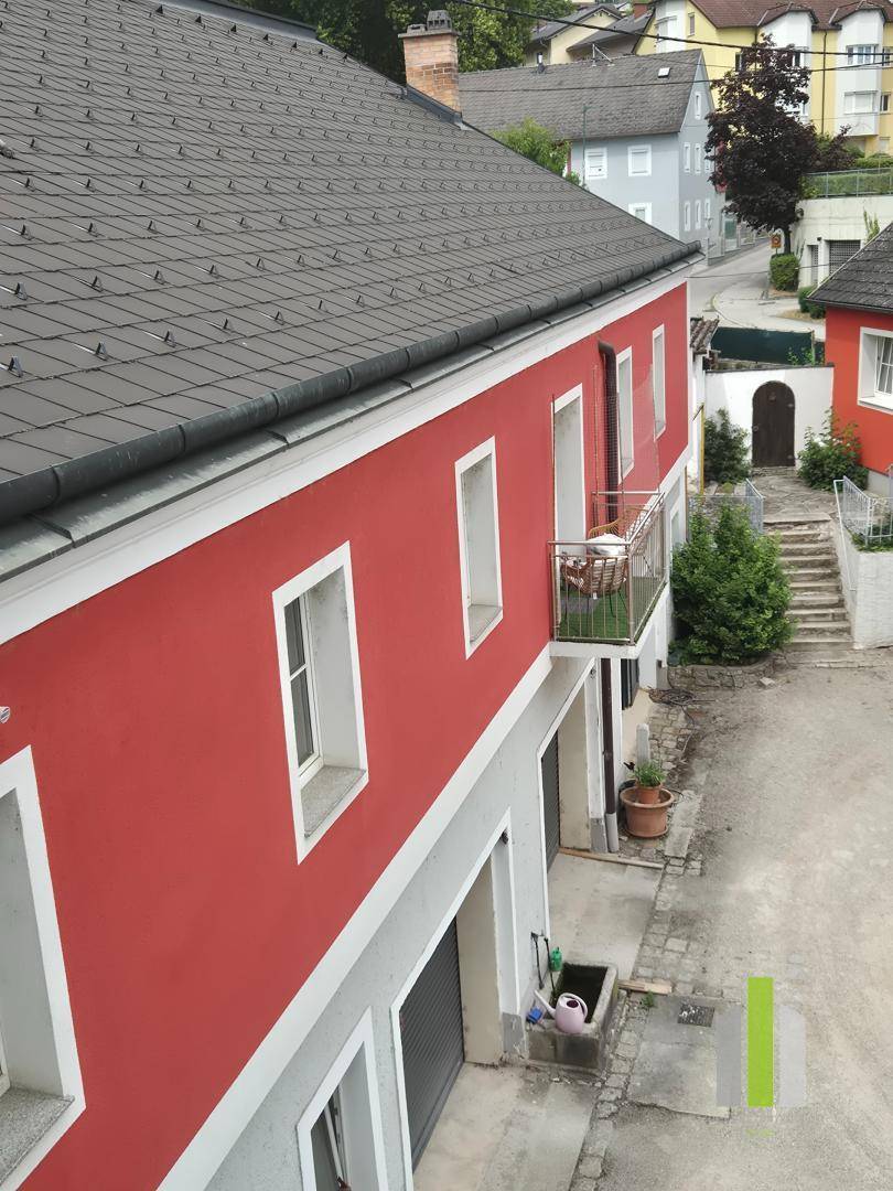 Seitenansicht eines roten Hauses mit Balkon und Blick auf die umliegende Nachbarschaft.