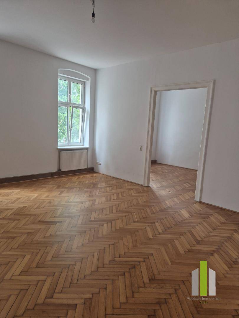 Geräumiges Zimmer mit Fischgrätparkett und offener Verbindung zu einem angrenzenden Raum.