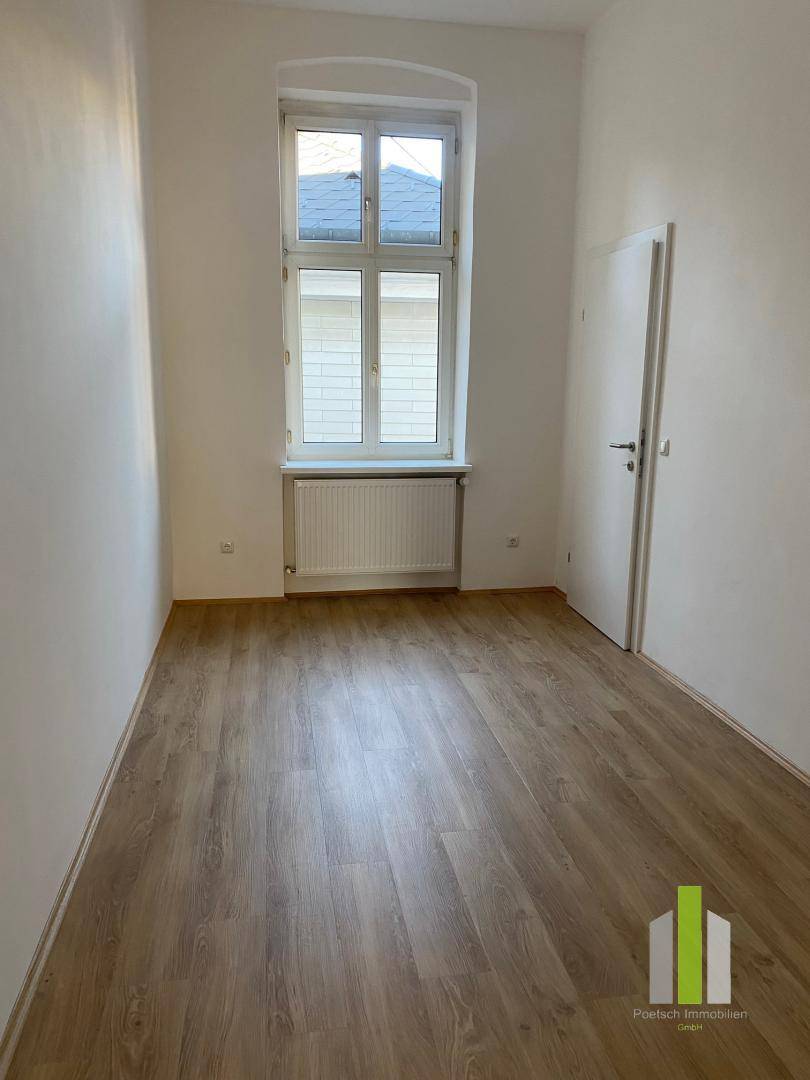 Kleines, helles Zimmer mit Laminatboden, einem Fenster und weiß gestrichenen Wänden.