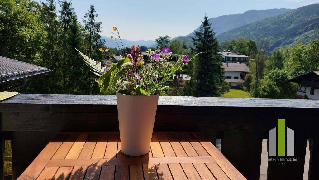 Balkon mit Holztisch und Blumen, der einen weiten Blick auf Berge und grüne Landschaft bietet.