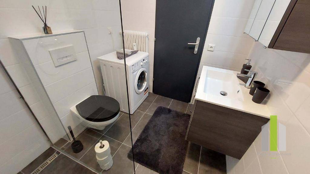 Modernes Badezimmer mit wandhängender Toilette, Waschbecken, Spiegelschrank und Waschmaschine.