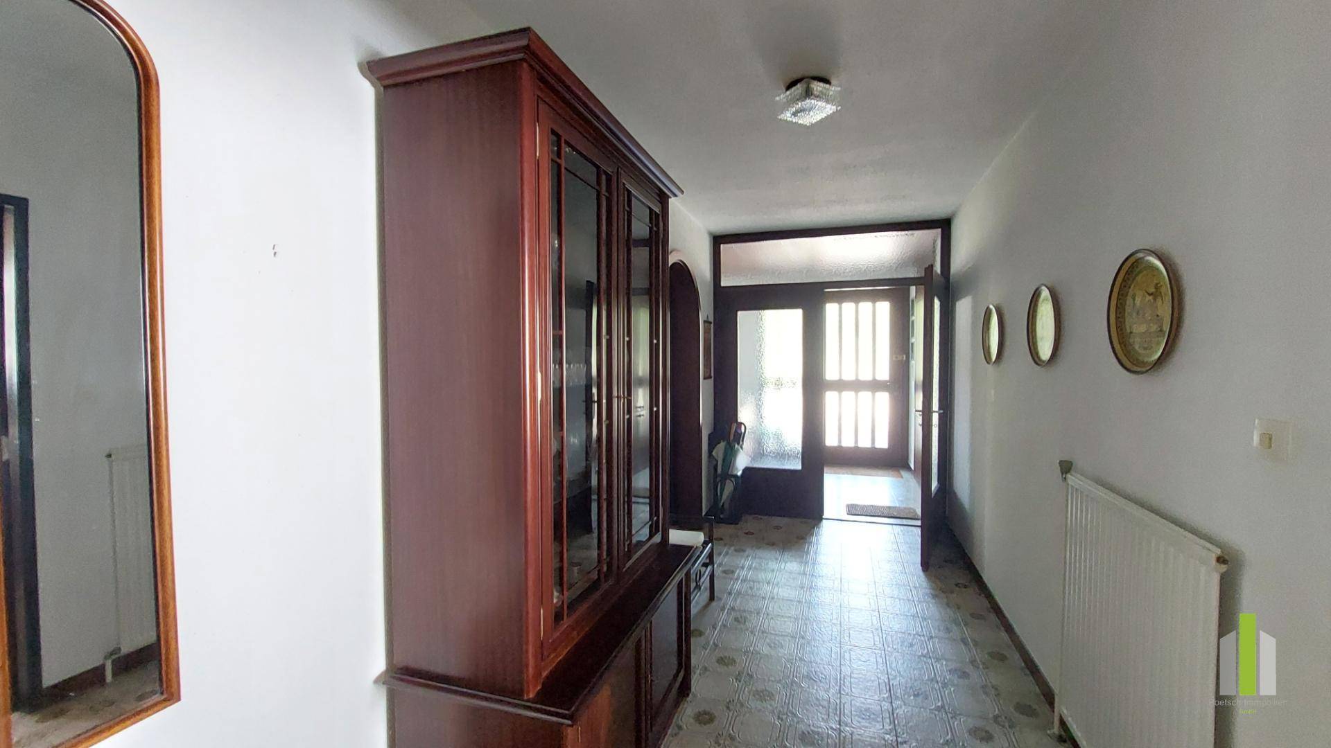 Eingangsbereich mit Fliesenboden, Holzschrank und Spiegel, der zur Haustür führt.