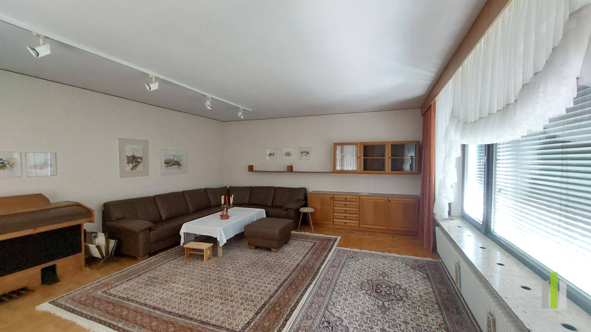 Geräumiges Wohnzimmer mit großer Eckcouch, Teppichen und Holzmöbeln, gut beleuchtet.