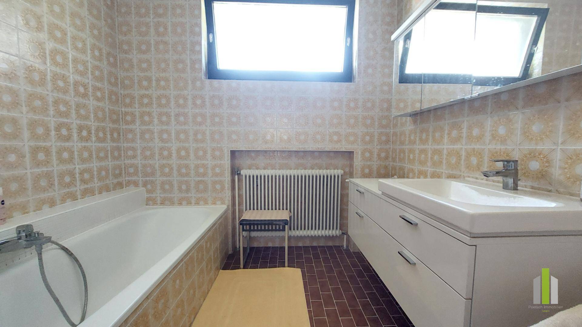 Badezimmer mit Badewanne, Waschbeckenunterschrank und Fenster, komplett gefliest in hellem Muster.