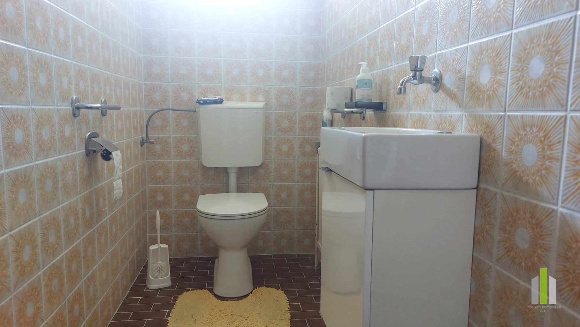 Kleines Gäste-WC mit gemusterten Fliesen, Toilette und Waschbecken in hellem Design.