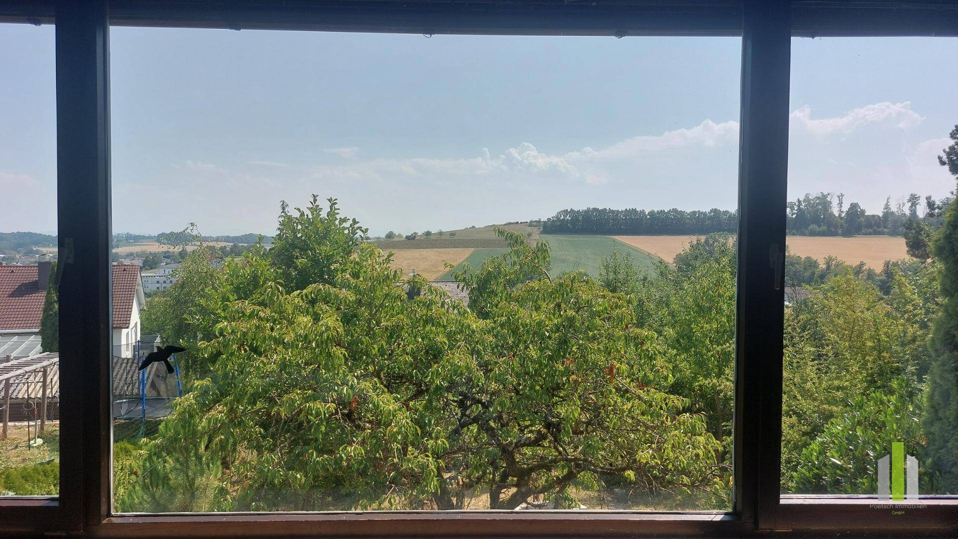 Weitblick aus dem Fenster des Wohnzimmers über grüne Felder und die umliegende Landschaft.