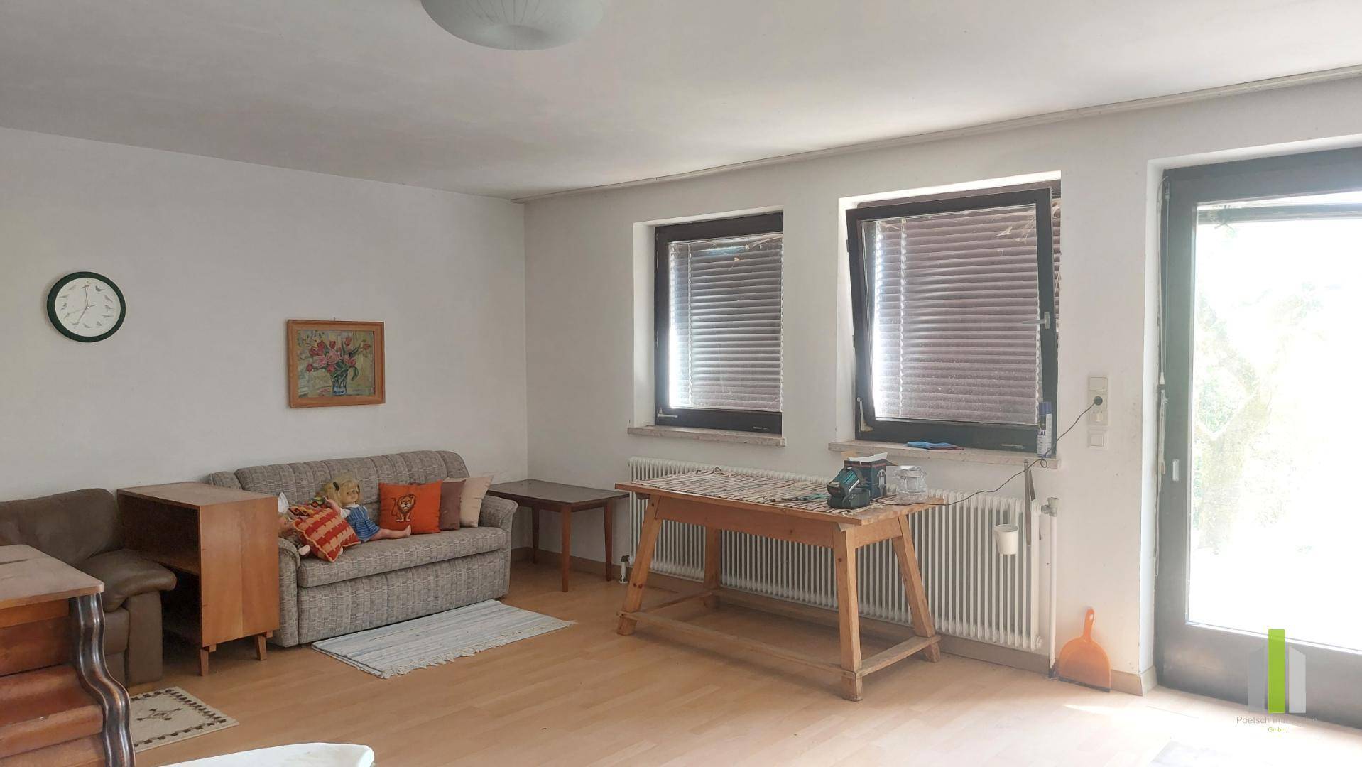Helles Wohnzimmer mit Sofa, Tisch und Fenstern, die viel Tageslicht hereinlassen.