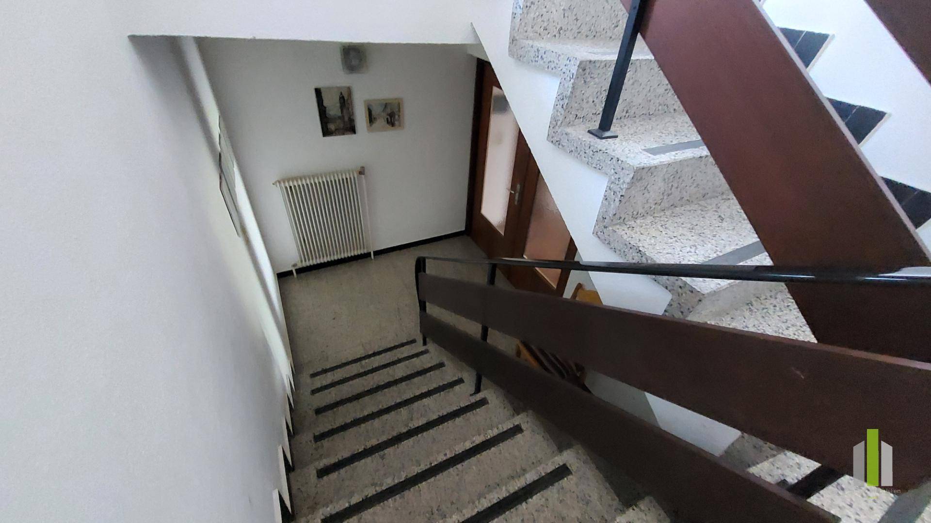 Treppenhaus mit Terrazzo-Stufen und Holzgeländer, das in die obere Etage führt.