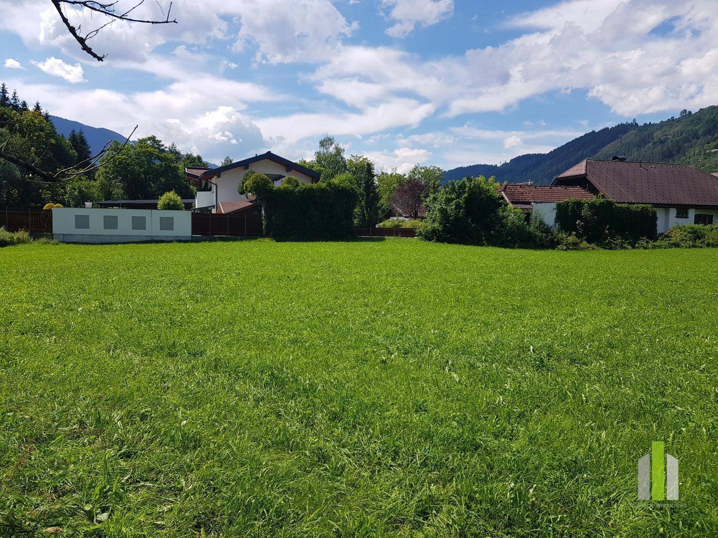 Großes grünes Feld mit freiem Blick auf die umliegende Natur und die angrenzenden Wohnhäuser.